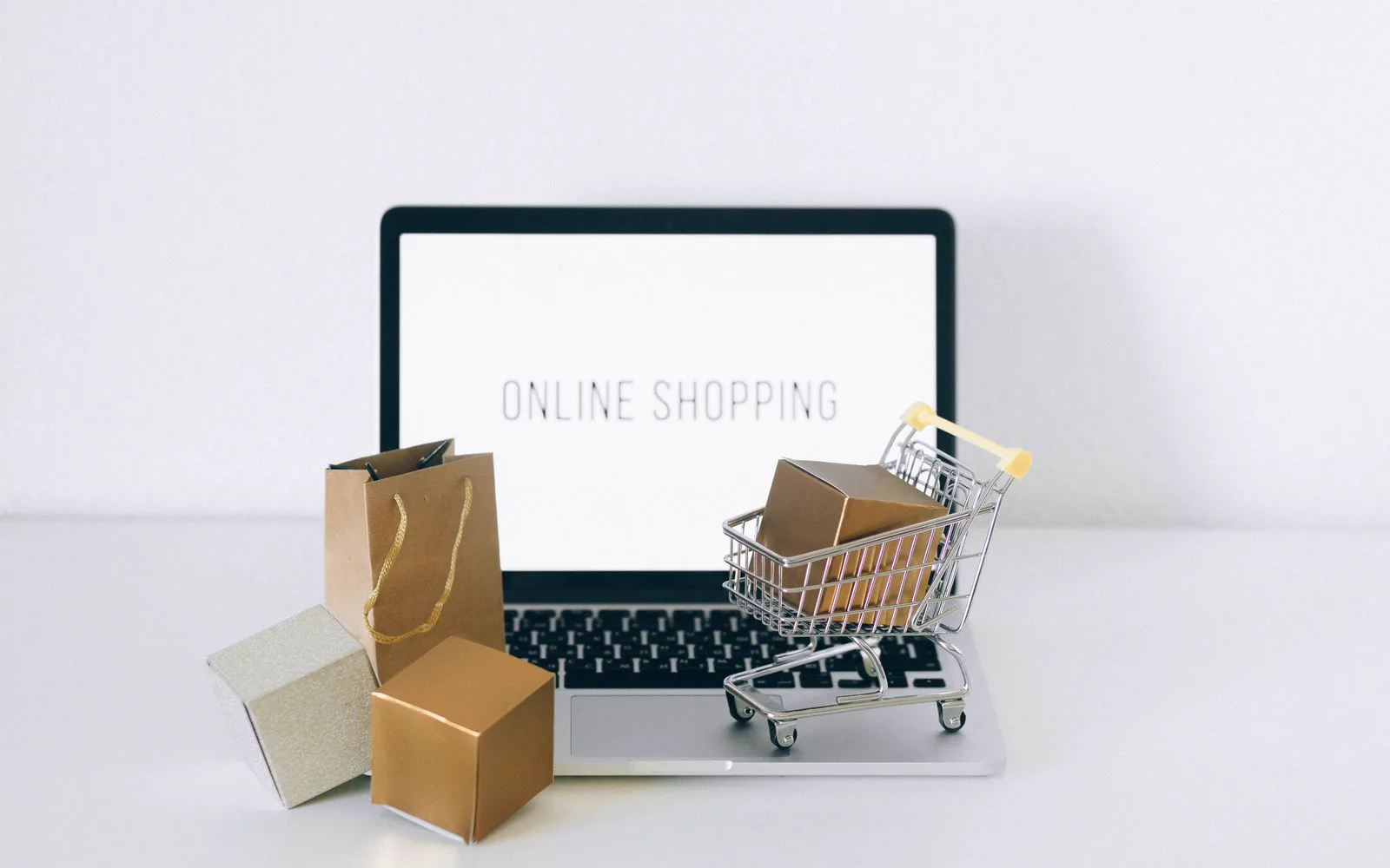 A laptop screen reading 'online shopping' beside gift boxes and a small shopping cart
